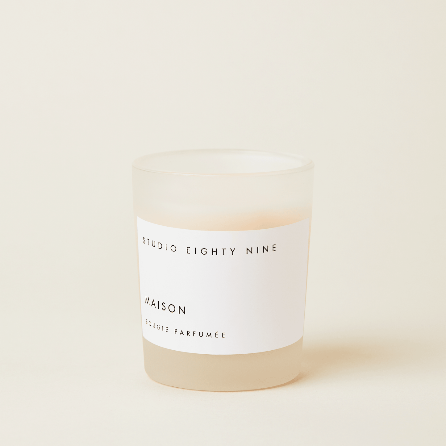 Petite-sized scented candle in frosted glass with beige-toned wax, featuring a white, minimalist rectangular horizontal label showcasing the brand 'STUDIO EIGHTY NINE', scent 'MAISON', and product 'BOUGIE PARFUMÉE' in clean uppercase typography.